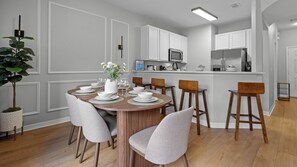 Eine moderne Küche mit weißen Schränken, ein Essbereich mit einem Holztisch und -stühlen sowie eine kleine Bar.