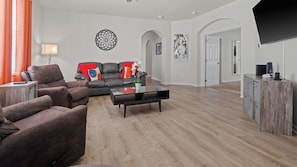 A living room with a sofa, armchairs, a coffee table, and a TV stand. - 4BR Near Disney at Trafalgar Village (Kissimmee)