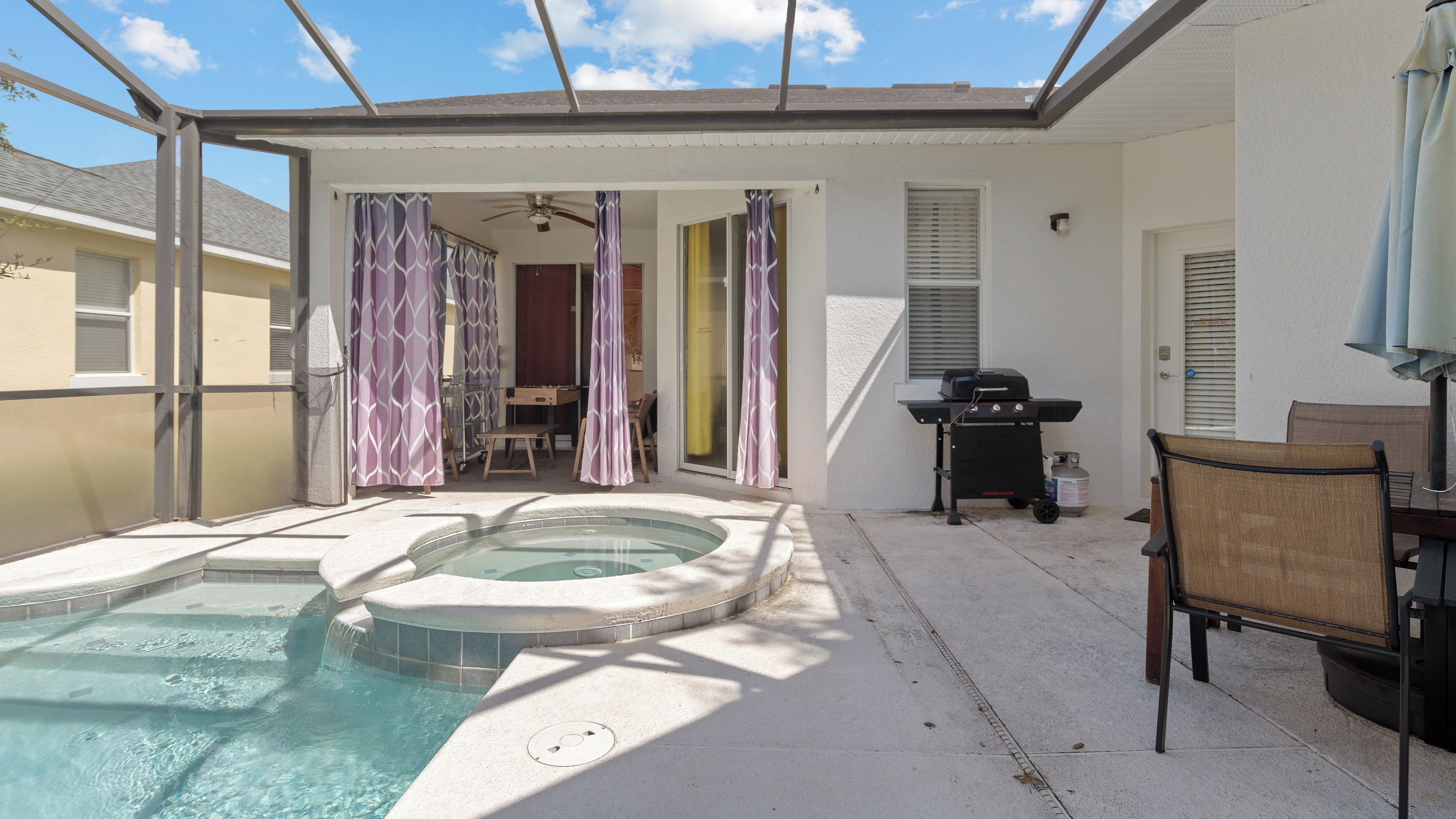 Een overdekt buitenzwembad met een jacuzzi, een barbecue en een tafel met stoelen.