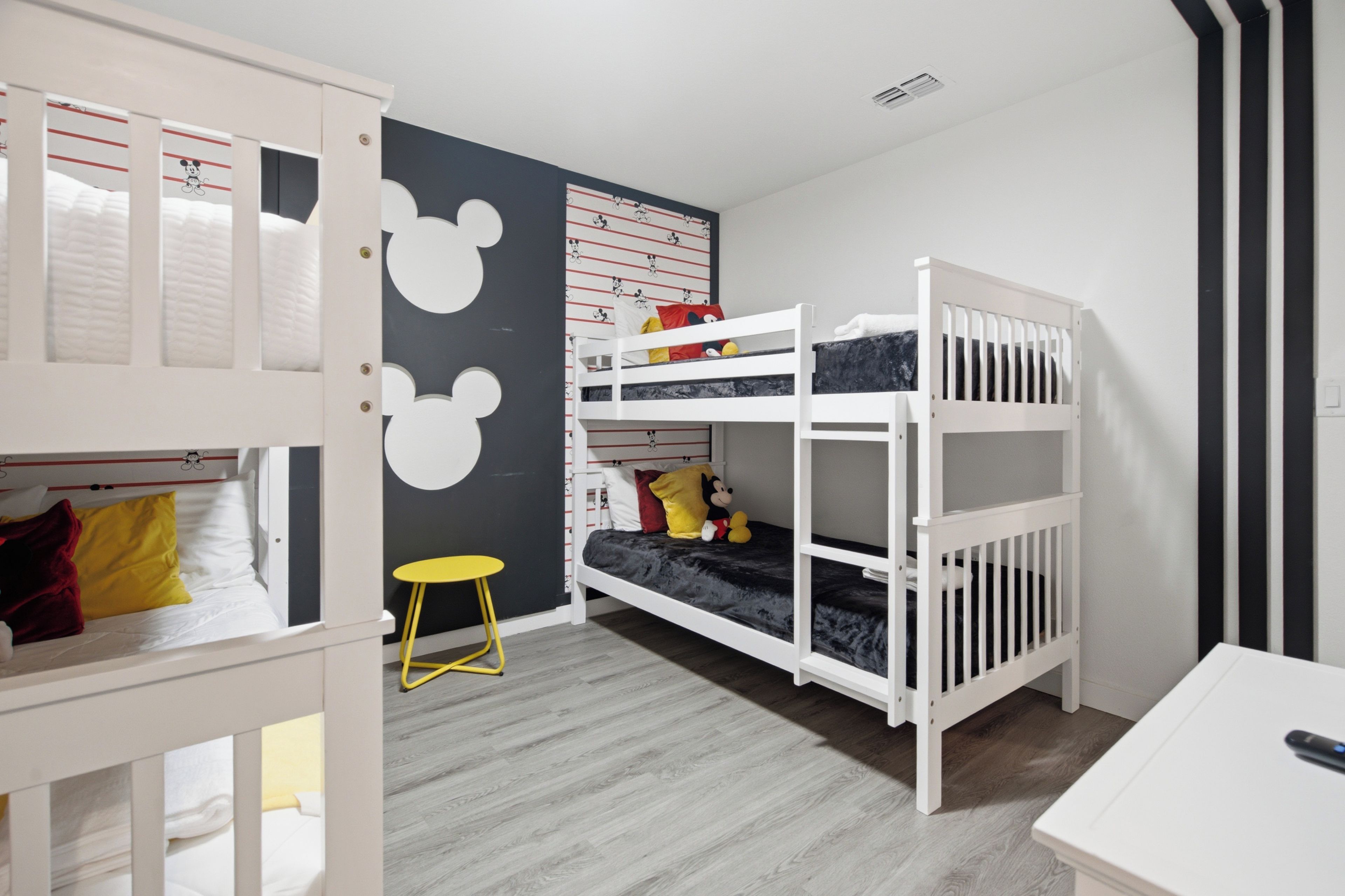 Ein Kinderzimmer mit Etagenbetten, einem kleinen Tisch und einer Wanddekoration mit Mickey Mouse.