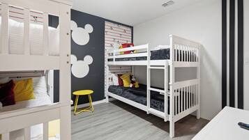 Ein Kinderzimmer mit Etagenbetten, einem kleinen Tisch und einer Wanddekoration mit Mickey Mouse.