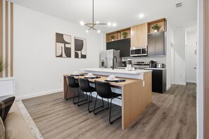 Eine moderne Küche mit einer zentralen Kochinsel, schwarzen Stühlen, einer Mikrowelle und einem Kühlschrank.