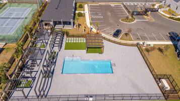 Ein Schwimmbad mit umlaufender Terrasse, ein Parkplatz und ein Gebäude mit flachem Dach.