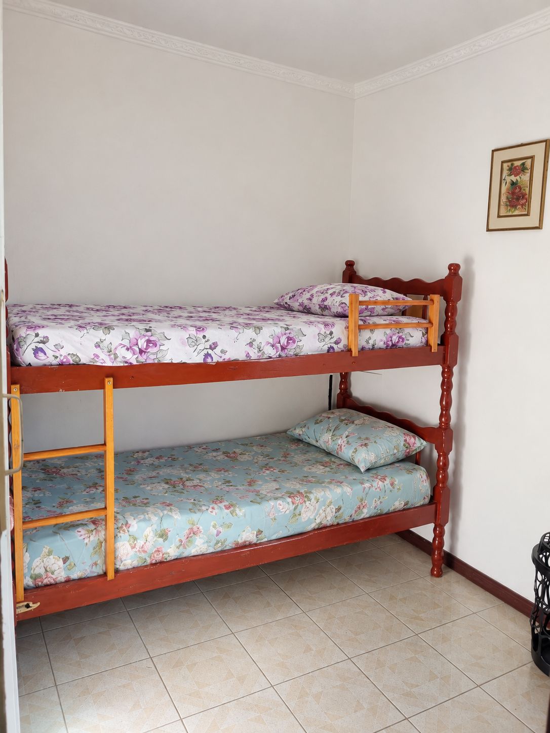 Uma cama de solteiro com roupa de cama florida em um quarto com piso de azulejos e um quadro na parede.