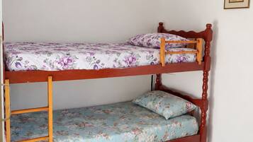 Uma cama de solteiro com roupa de cama florida em um quarto com piso de azulejos e um quadro na parede.