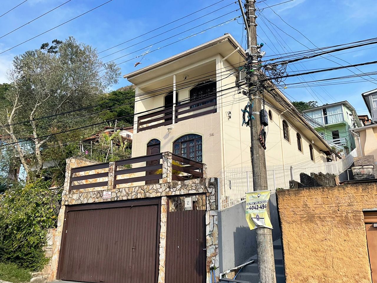 Um edifício de dois andares com varanda, entrada protegida por grades e um poste de eletricidade com vários fios.