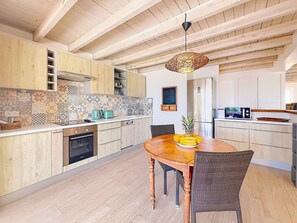 A modern kitchen with wooden cabinets, a dining table with chairs, and a hanging light fixture. - Villa Les Alizés – Pinel Island View, Private Pool (Marigot)