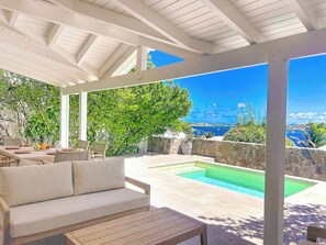 A covered outdoor seating area with a pool and a view of the ocean. - Villa Les Alizés – Pinel Island View, Private Pool (Marigot)