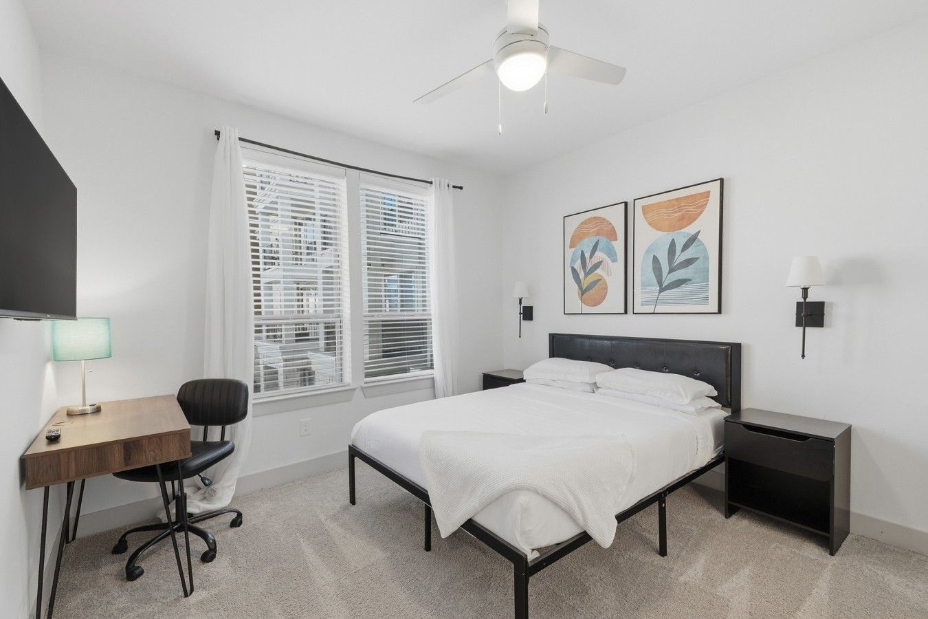 Quarto com cama, escrivaninha, cadeira, mesas de cabeceira e obras de arte.