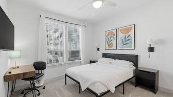 Quarto com cama, escrivaninha, cadeira, mesas de cabeceira e obras de arte.