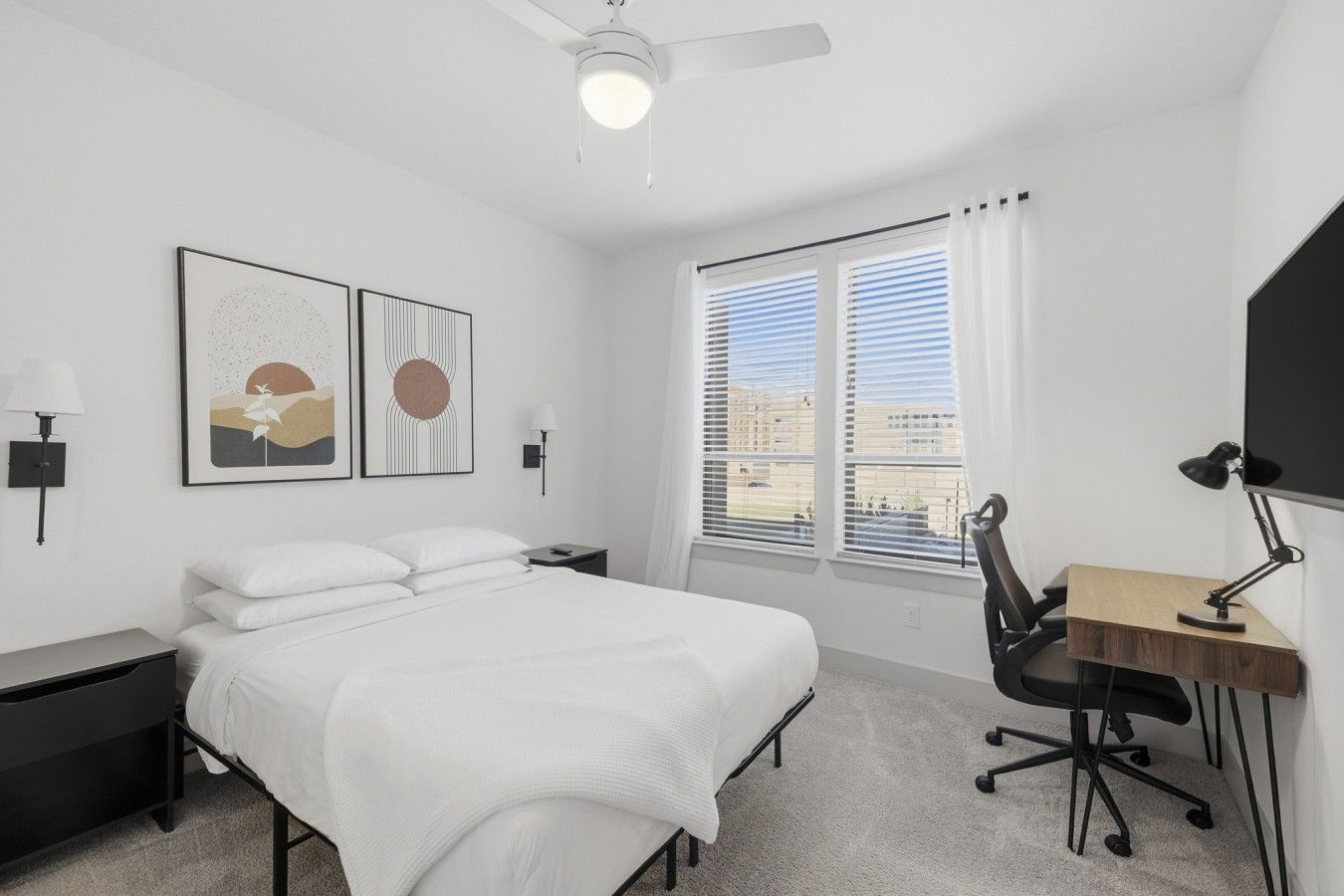 A modern bedroom with a bed, desk, chair, and artwork on the wall.