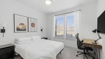A modern bedroom with a bed, desk, chair, and artwork on the wall.