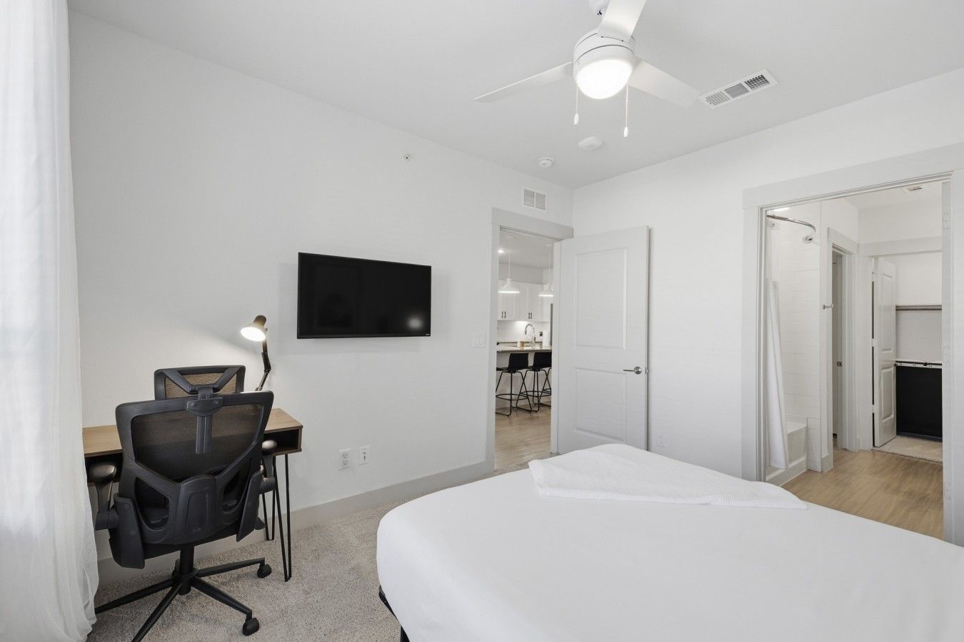 A hotel room with a bed, desk, chair, TV, and a ceiling fan.