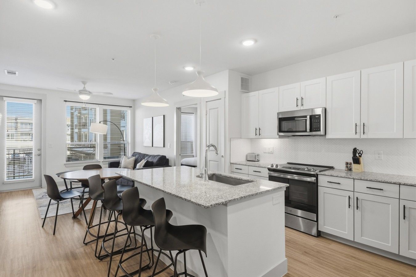 A modern kitchen with white cabinetry, a granite countertop island, and a stainless steel range hood.