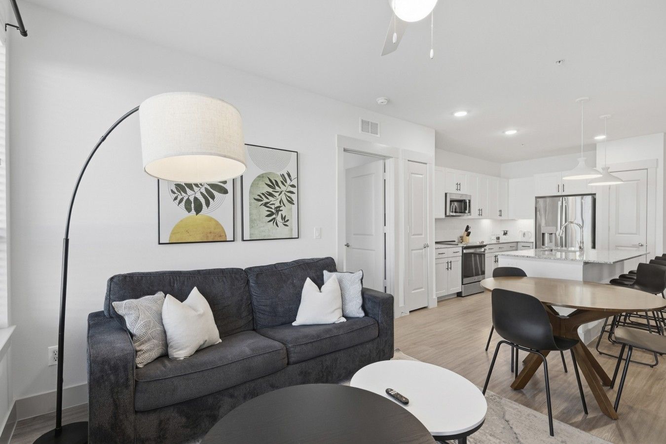 A modern living room with a sofa, a dining table, and a kitchen in the background.