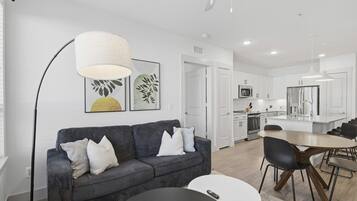 A modern living room with a sofa, a dining table, and a kitchen in the background.