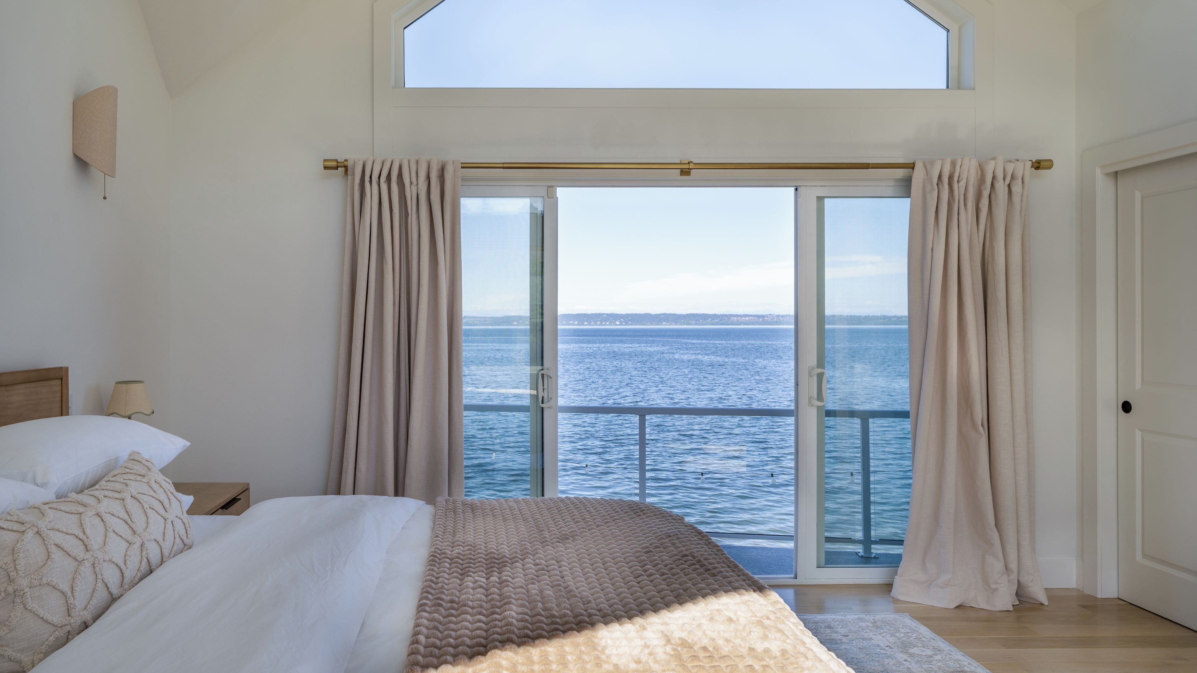 Un dormitorio con una cama grande, vista al mar a través de un ventanal corredero y un tragaluz.
