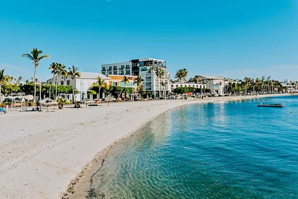Un hôtel situé en bord de mer, doté d’une piscine, de palmiers et surplombant un ciel bleu azur.