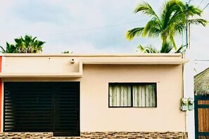 A two-story building with a flat roof, a window with decorative bars, and a door with a wooden frame. - Casa Madero #3, 1 block from the Malecón (La Paz)