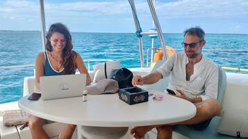 Dos personas sentadas a una mesa redonda en un barco, con una computadora portátil y una caja de pañuelos.