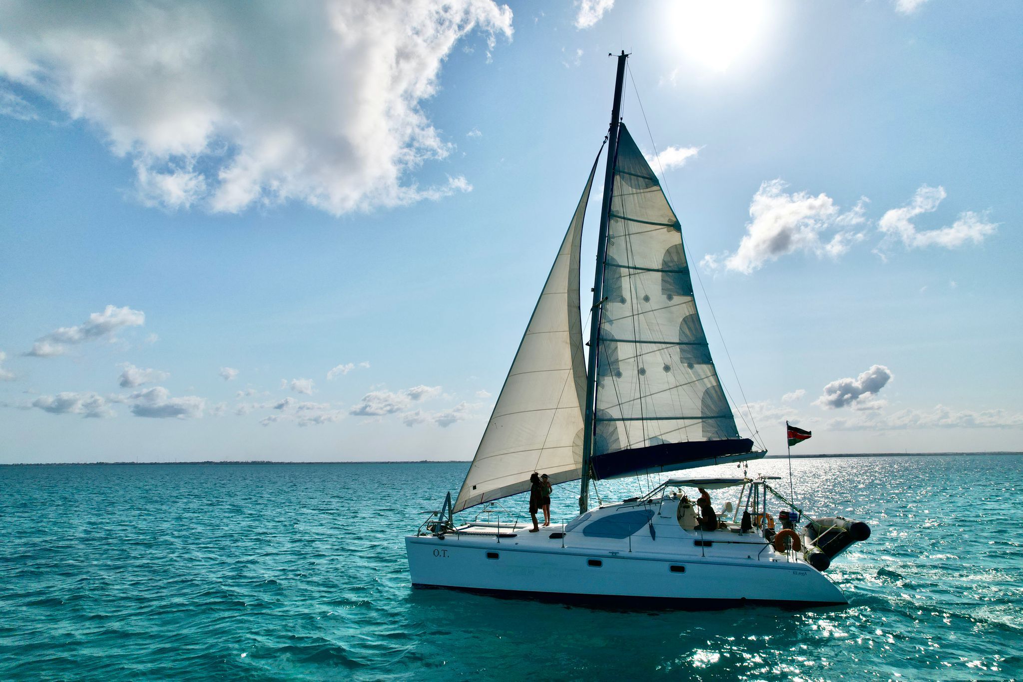 Un velero con un solo mástil y una persona de pie en la popa.