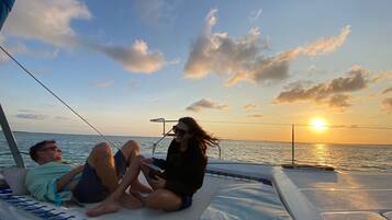 Una pareja descansando en la cubierta de un barco con vista a la puesta de sol sobre el agua.