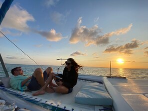 A couple relaxing on a boat deck with a view of the sunset over the water.
