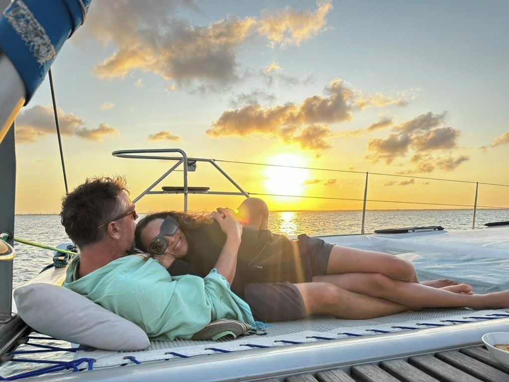 Un couple se détend sur des chaises longues sur le pont d’un bateau, avec un coucher de soleil en arrière-plan.
