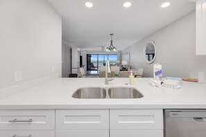 A modern kitchen with a double sink, white cabinetry, and a view to the dining area. - Pelicans Roost 303 – Beautifully Remodeled Beachfront Escape with Gulf Views & H (Sanibel)