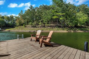 Eine hölzerne Mole mit zwei Adirondack-Stühlen, die auf einen ruhigen See blicken, umgeben von dichtem Wald.