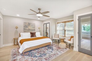 A modern bedroom with a bed, a ceiling fan, a large window, and a view of the outdoors. - Charming 3-bedroom lakehouse in Hartwell with plenty of outdoor living space (Hartwell)