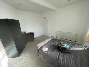 A bedroom with a bed, a wardrobe, a radiator, and a door. - Cozy Cannock Retreat - 3 Bedroom 2 Bathroom (Cannock)
