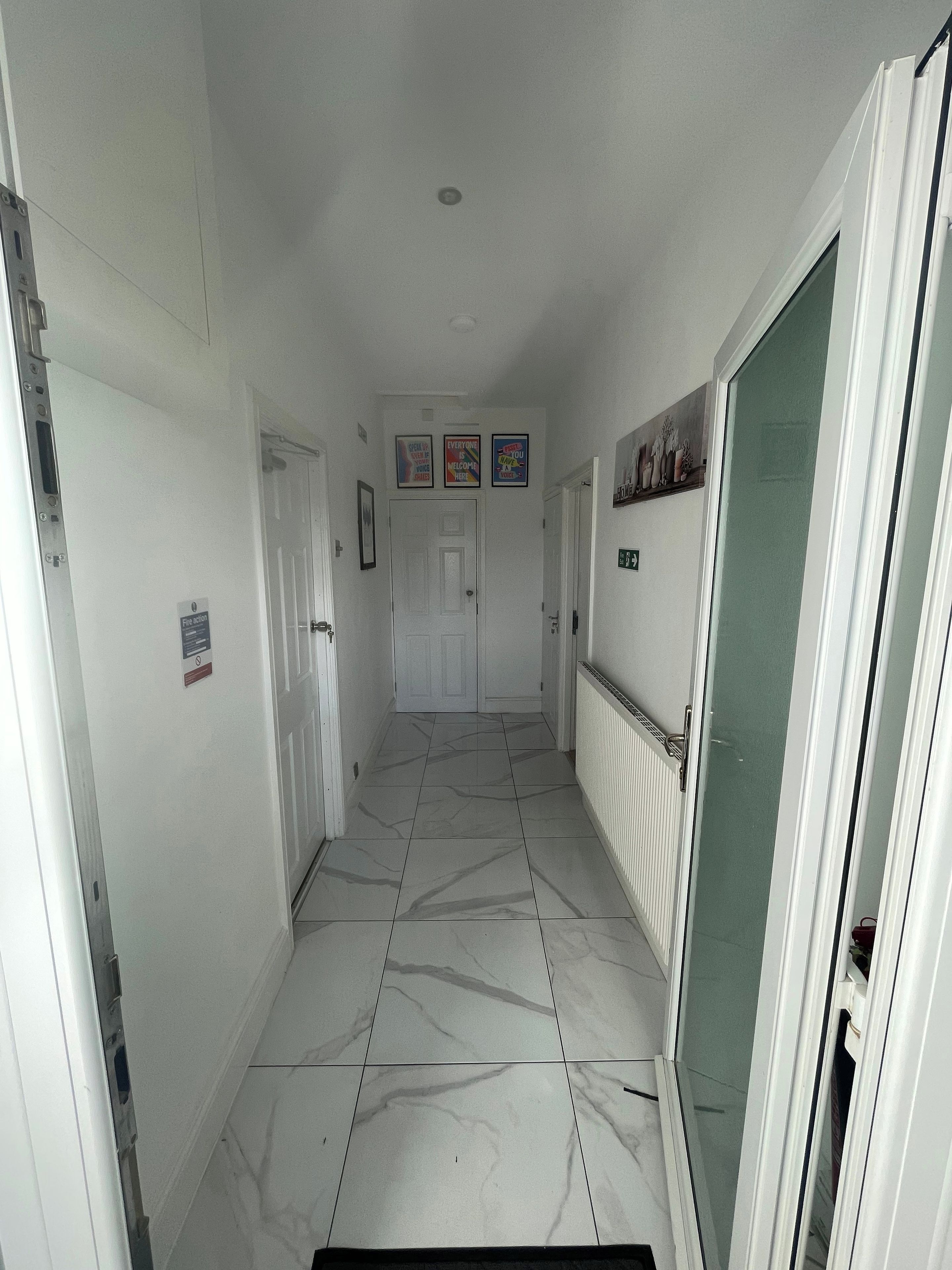 A hallway with white walls, a tiled floor, and a door at the end.