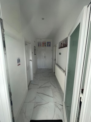 A hallway with white walls, a tiled floor, and a door at the end. - Cozy Cannock Retreat - 3 Bedroom 2 Bathroom (Cannock)