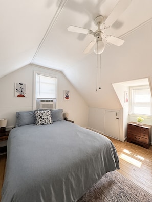 Un dormitorio con cama, ventilador de techo, ventana y cómoda.