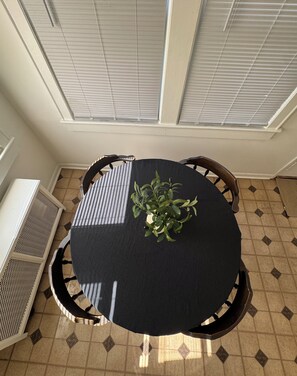 A round table with a dark tablecloth, surrounded by wooden chairs, in a room with patterned floor tiles and a window with blinds. - Charming 3-bedroom 2- bathroom house with AC in South Plainfield (South Plainfield)