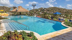Ein Swimmingpool mit überdachter Strohdachkonstruktion, Liegestühlen und Blick auf eine Hügellandschaft.