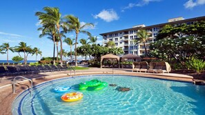 Ein Pool mit Liegestühlen und Palmen, umgeben von einem Gebäude mit mehreren Balkonen.