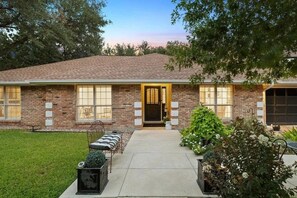 A brick house with a front porch, a garage, and a well-maintained lawn. - Two bedroom Westlake house, very convenient to downtown and Zilker / ACL (Austin)