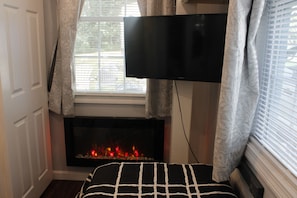 Ein Zimmer mit Kamin, darüber angebrachtem Fernseher und einem mit Vorhängen drapierten Fenster.