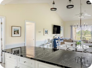 A kitchen with a marble countertop, white cabinetry, a dining area with white chairs, and a ceiling fan. - Sunny Golf Course Condo Pool - 8 Min. To Beach! With AC (Myrtle Beach)