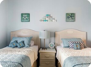 Un dormitorio con dos camas, cada una con cabecera, una mesita de noche con lámpara y decoración en la pared.