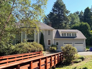 A two-story house with a garage, surrounded by greenery and a wooden bridge. - Beautiful 2-bedroom apartment in welcoming Newton neighborhood (Newton)
