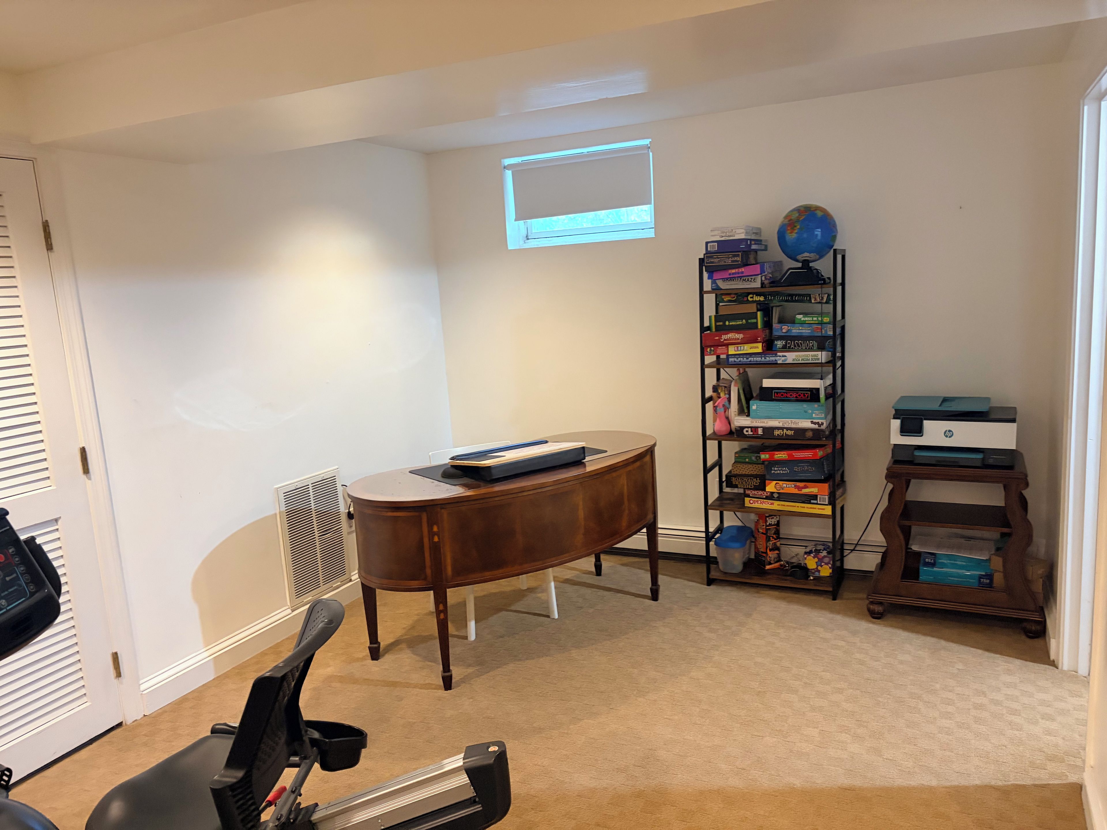 Un bureau à domicile équipé d’un bureau, d’une chaise, d’un tapis de course, d’une bibliothèque et d’une fenêtre avec des stores.
