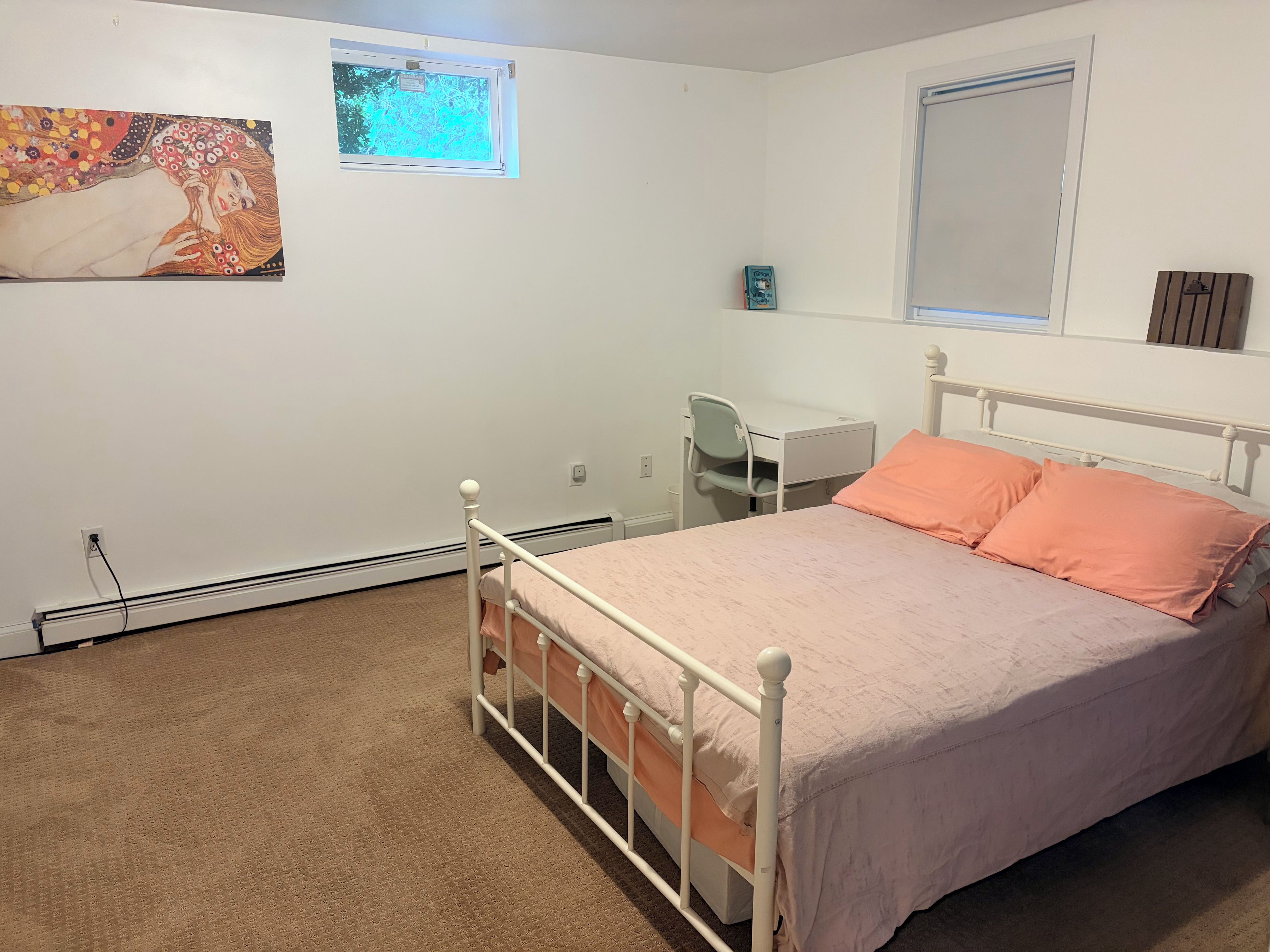 A bedroom with a bed, a desk, and a chair. There is a window with a view of trees.