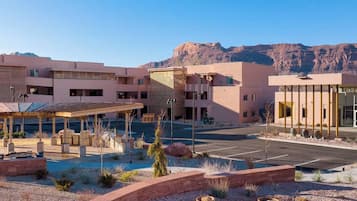 A multi-story hotel with a covered parking area, outdoor seating, and a view of mountains.
