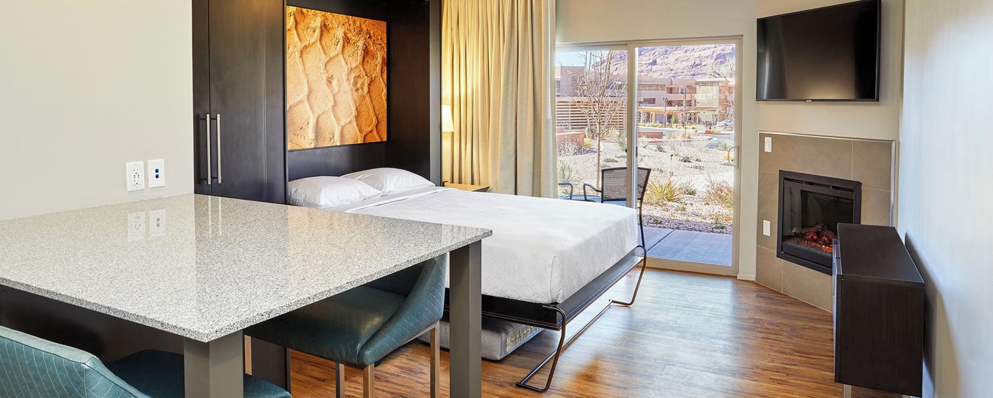 A hotel room with a bed, a desk, a TV, a fireplace, and a view of the outdoors.