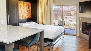 A hotel room with a bed, a desk, a TV, a fireplace, and a view of the outdoors.