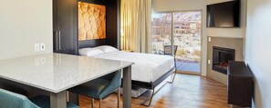 Habitación de hotel con cama, escritorio, televisión, chimenea y vista al exterior.