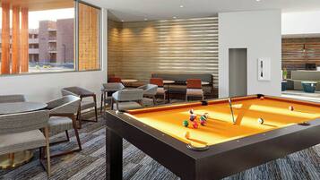 A pool table in a room with a view of a building outside. There are chairs and a sofa in the room.